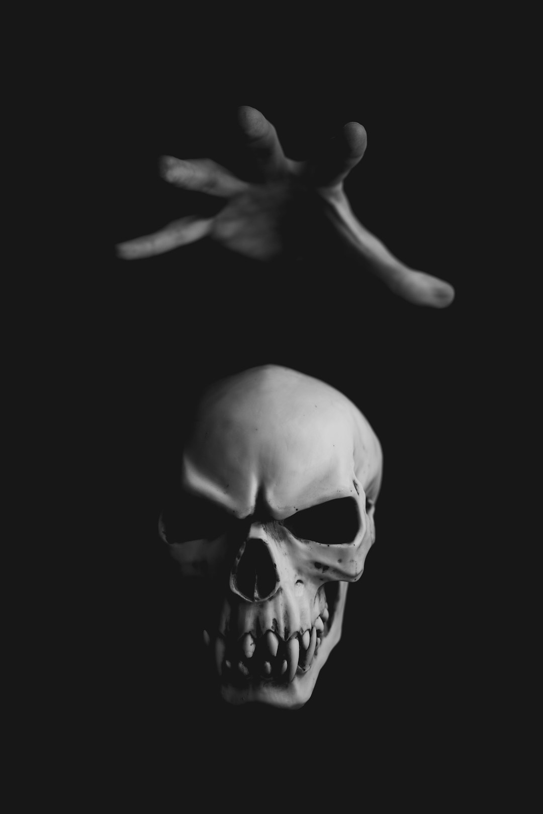 A white skull floating in the air with one hand reaching out from behind it against a black background, in the style of horror, minimalistic, monochrome, hyper realistic, cinematic, realism. –ar 85:128