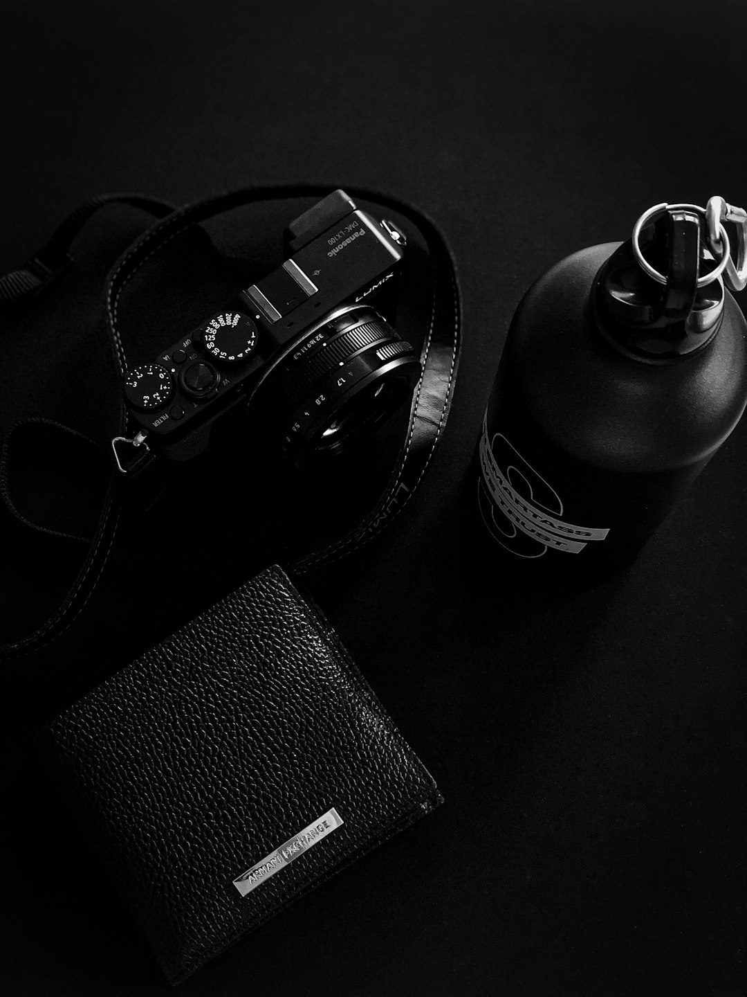 Black and white photography of the product photo, camera with leather strap, black metal bottle in minimalistic modern style, on top is placed an open men’s wallet with money inside, all elements lie flat on a dark background, minimalism, minimal design, high resolution, high contrast, high quality, high detail, cinematic light, sharp focus, shot by Hasselblad H6D400c medium format camera –ar 3:4