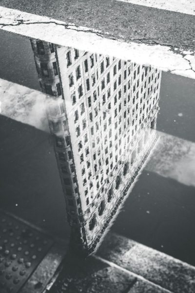 Black and white street photography of the Flatiron Building reflected in a puddle in New York City, in the style of the 1920s. --ar 85:128