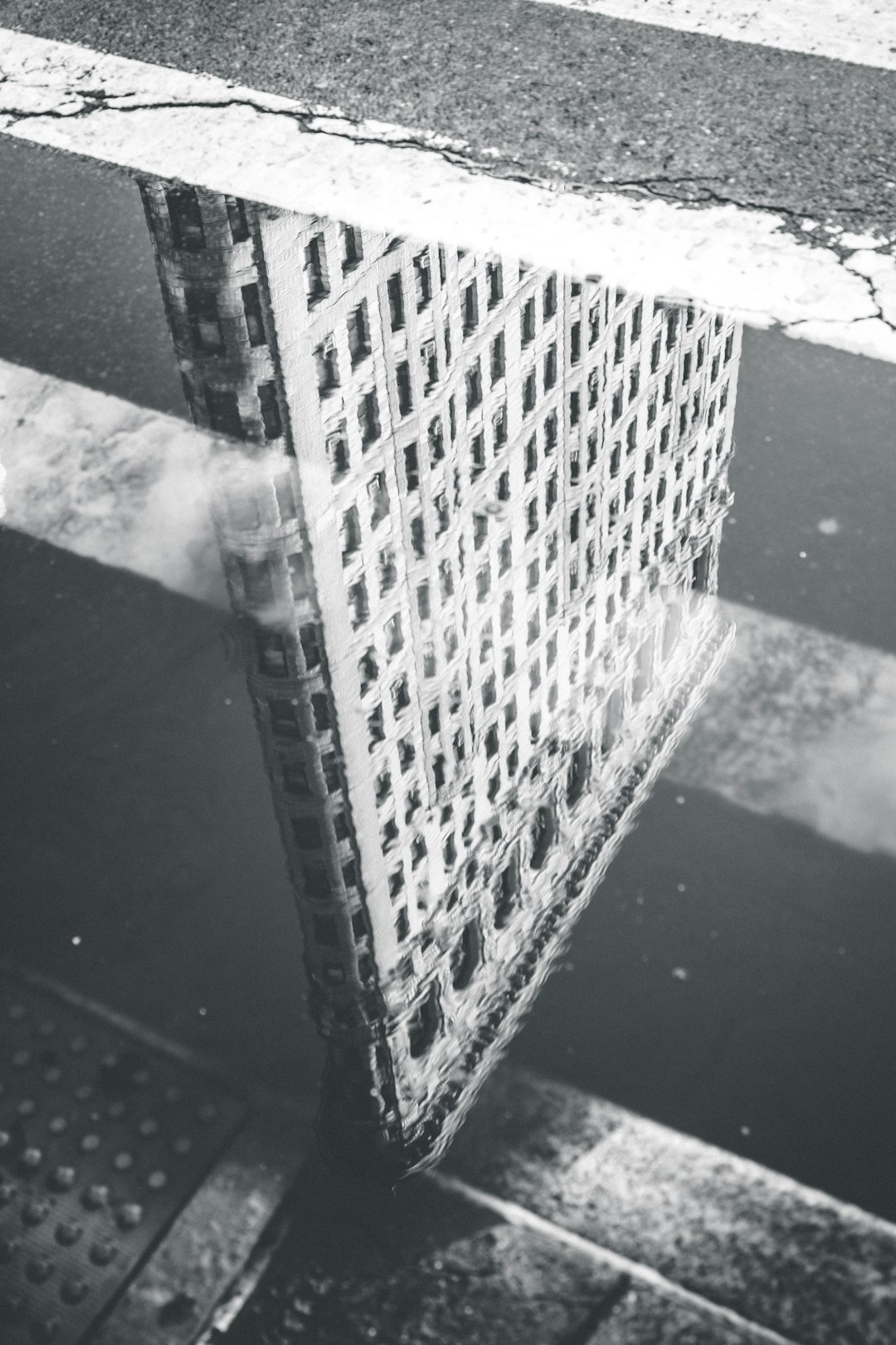 Black and white street photography of the Flatiron Building reflected in a puddle in New York City, in the style of the 1920s. –ar 85:128