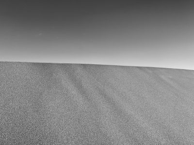 A black and white photograph of the top half of an endless sand dune, with a clear sky in the background. The grainy texture of fine sand is visible against the stark contrast between light gray and dark grey hues. A minimalist composition focusing on simplicity and elegance. --ar 4:3