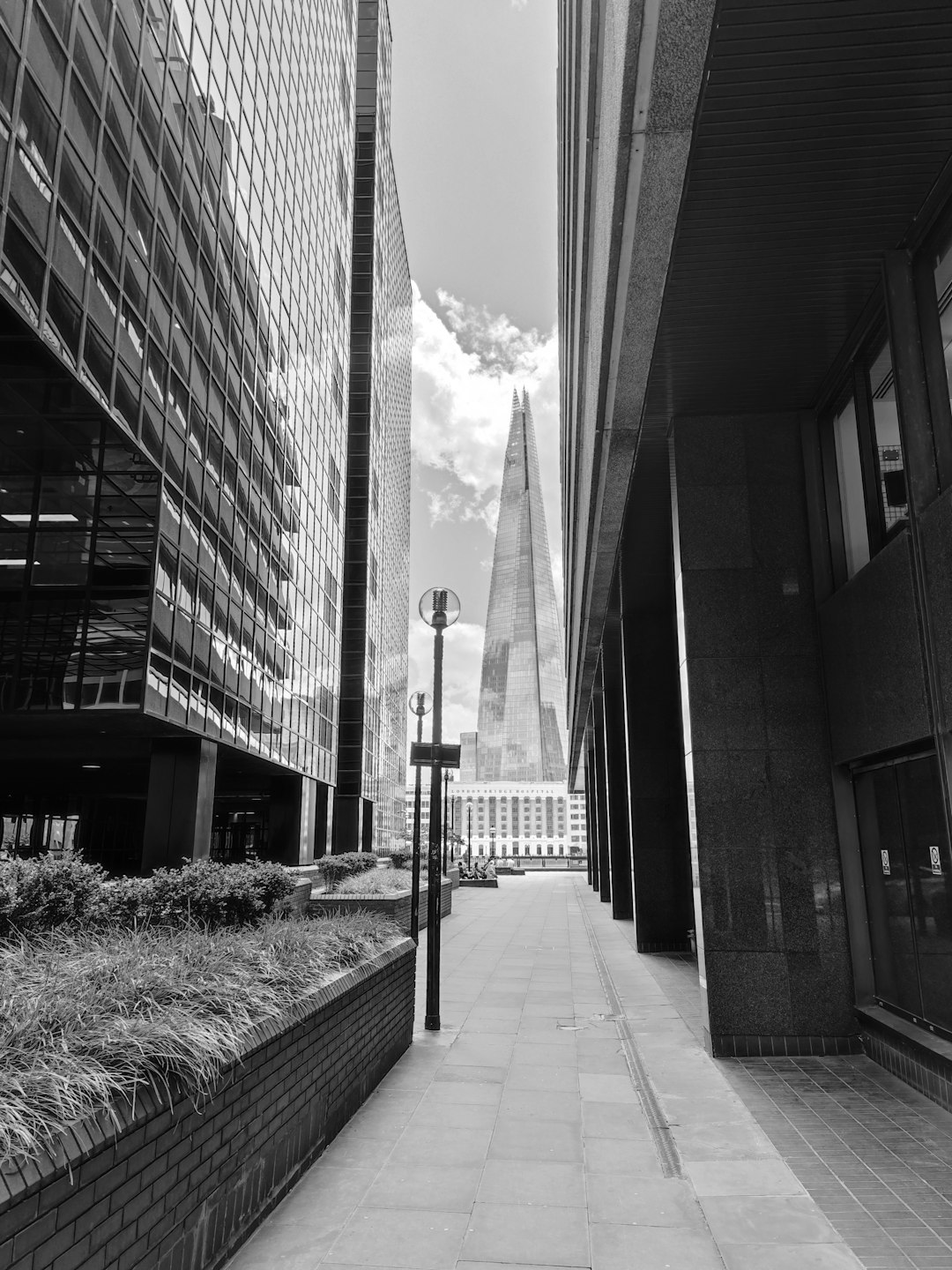 The black and white photograph of the small street leading to The Guidelines building in London with a view of the Shard tower, the photo taken from sidewalk level, with no people or cars visible, captured in the style of Hasselblad X1D camera. –ar 3:4