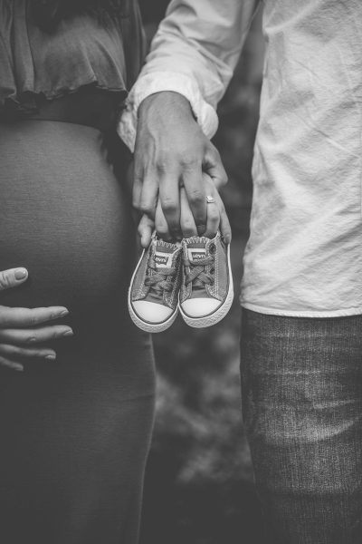 Black and white photography of a pregnant woman holding her husband's hand while showing off Converse shoes on her belly, with highly detailed style. --ar 85:128