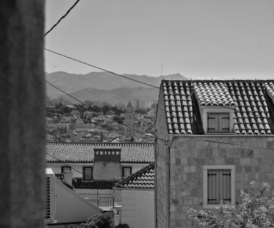 Photo of S throughout the city, in black and white, with a view from one house to another roof with tiles, behind which you can see some mountains in the distance. In the background we have many buildings that make up the entire town of split, which is located on top of hills. You will also be able to read about other places where it would create an interesting atmosphere for photography. The photo was taken during daylight, so all details were clearly visible. --ar 64:53