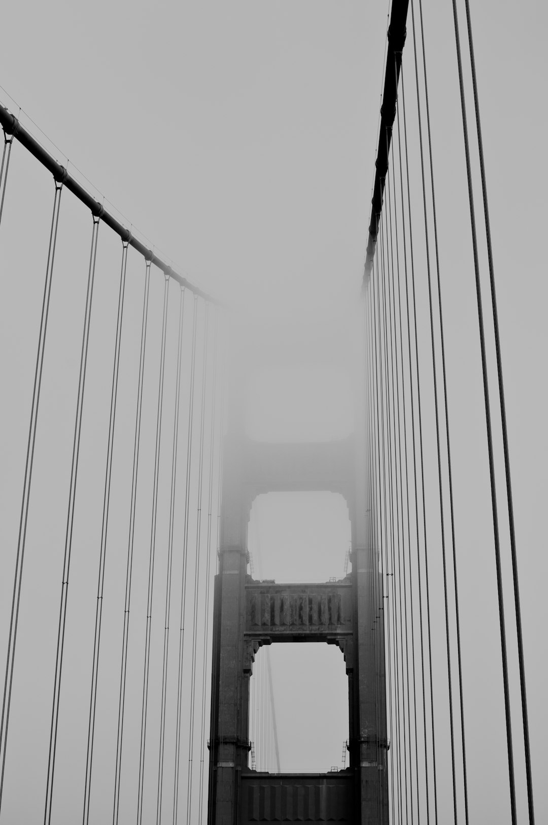 A black and white photo of the Golden Gate Bridge on a foggy day, looking up at the top left side of it. The photo appears to be in the style of [Ansel Adams](https://goo.gl/search?artist%20Ansel%20Adams). –ar 85:128