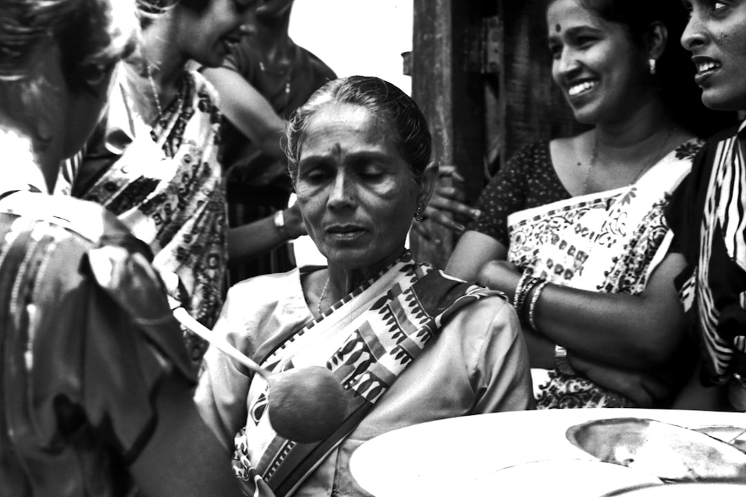 Black and white street photography of an Indian woman playing the traditional musical instrument veena, with other women smiling around her in monochromatic colors. The photograph is in the style of V.bytes. –ar 128:85