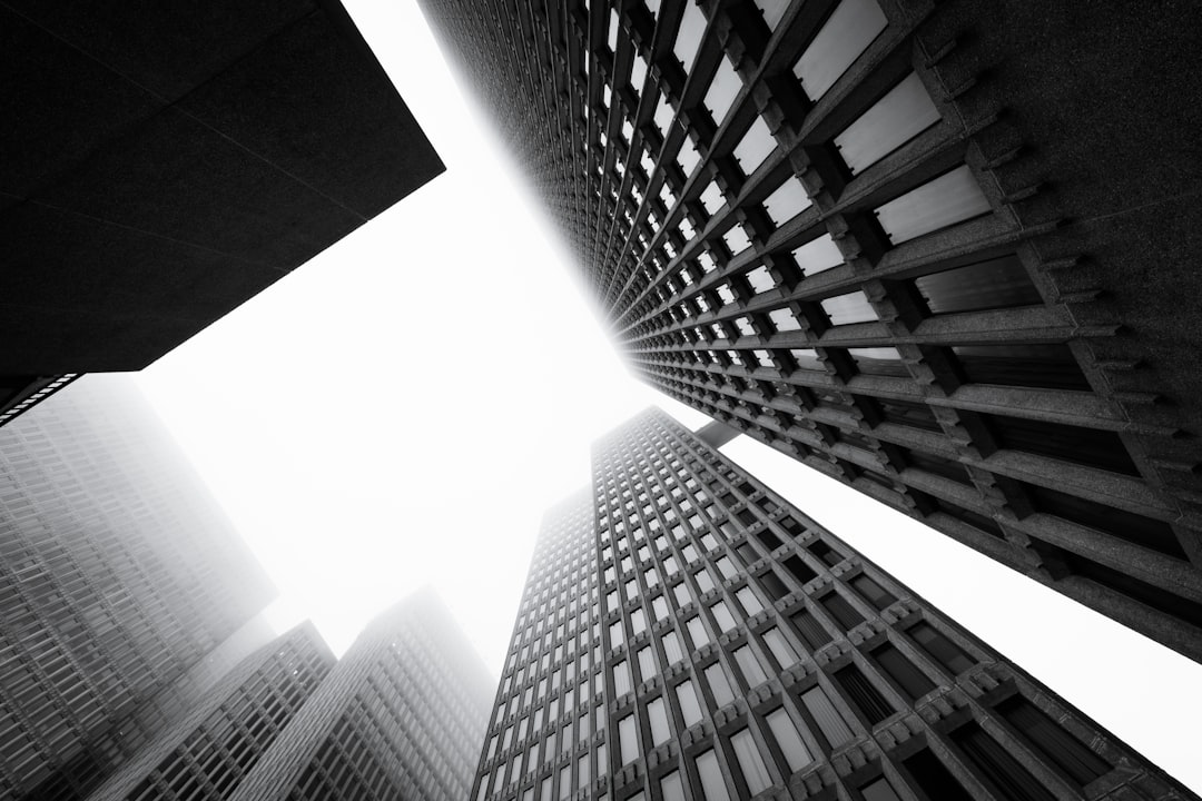 A black and white photograph of the exterior of tall buildings in downtown Montreal, with fog rolling through the streets, emphasizing their architecture. The focus is on the architectural details visible from below, with a clear sky above. High resolution photography, taken in the style of Sony Alpha A7 IV with a hyper realistic water light color atmosphere. –ar 128:85