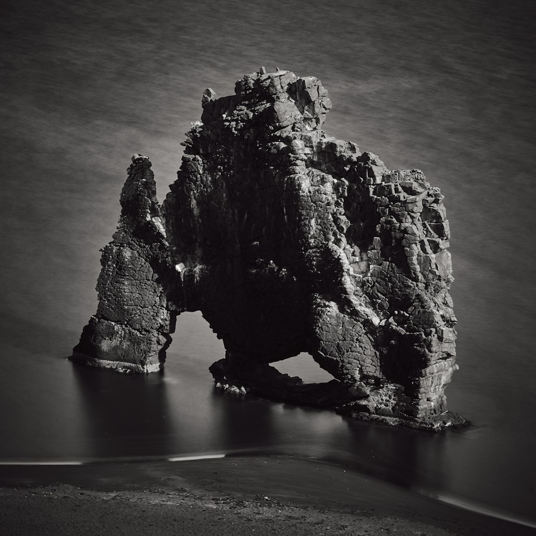 Icelandic sea stacks, Shrogge rock in the shape of an archway byFlat black water , captured with Sony Alpha A7 III and a macro lens, highlighting its unique structure against the dark background, National Geographic photo style, black & white photo