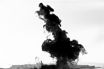 Black ink in water, white background, suspended in the air, swirling and forming into an abstract shape of upsidedown mountain with cloudlike smoke at its top. The scene is minimalist yet powerful, capturing the fluidity and elegance of black paint in motion against a stark backdrop. This image conveys mystery and depth, drawing inspiration from the photography style of Yann ArthusBertrand. --ar 128:85