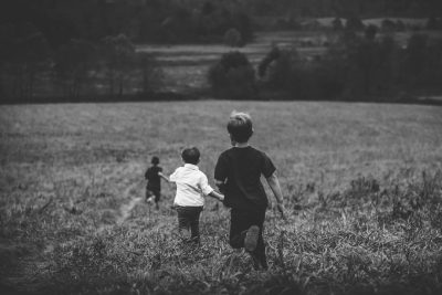 A black and white photo of two boys playing tag in a field, with other kids watching from the distance. The photo is in the style of [Ansel Adams](https://goo.gl/search?artist%20Ansel%20Adams). --ar 128:85