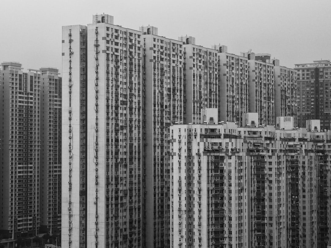 A black and white photo of an apartment complex in Hong Kong with tall buildings. The picture is taken from above, showing multiple multistory buildings side by side, all made of concrete. The buildings have windows on their sides and they form one big building with many doors and balconies. The city has no trees or greenery, it’s overcast and there seems to be some fog around. The shot looks very realistic and detailed, in the style of a Canon R50mm f/28 lens. –ar 4:3