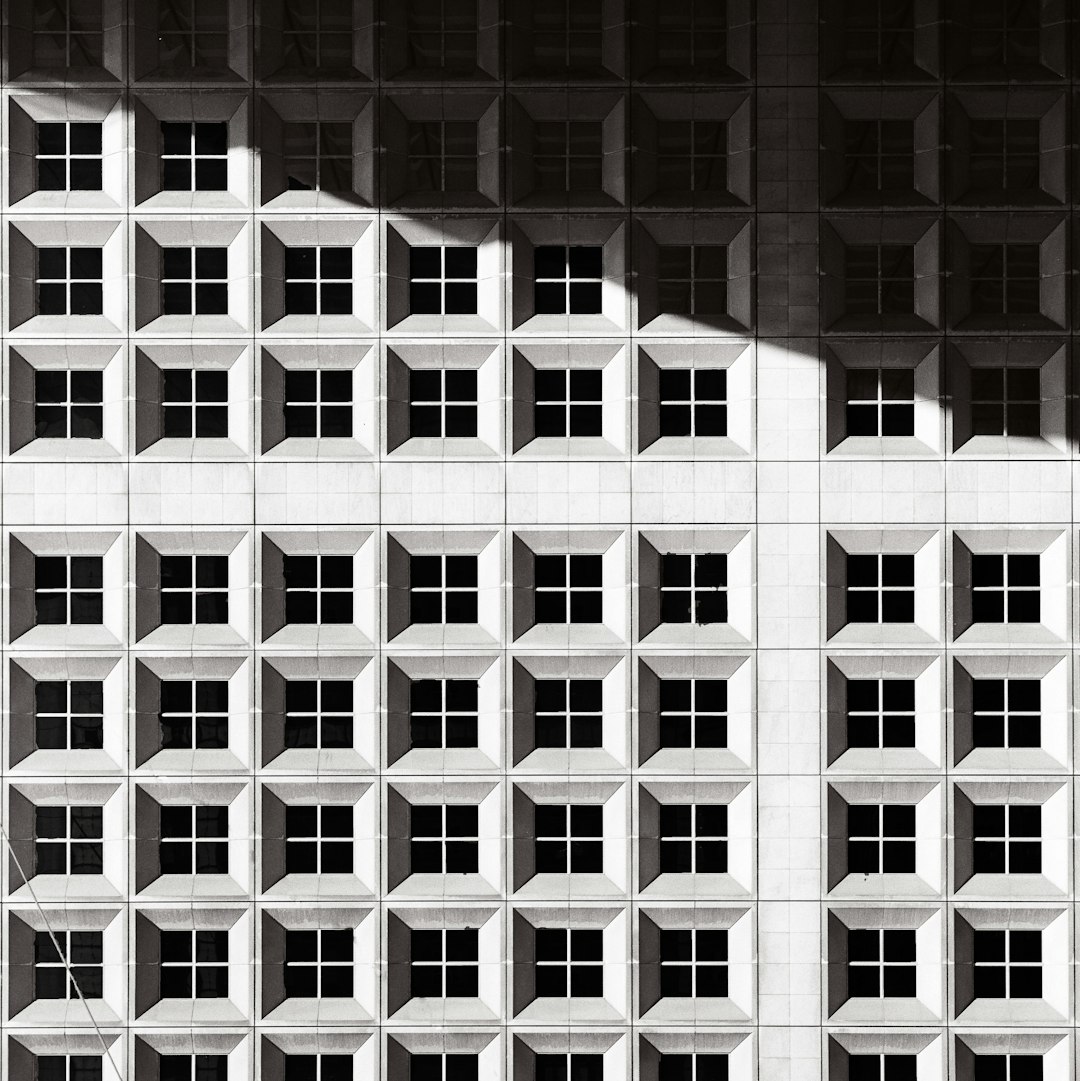 black and white geometric grid building facade, shadows cast on wall, architectural photography –ar 127:128