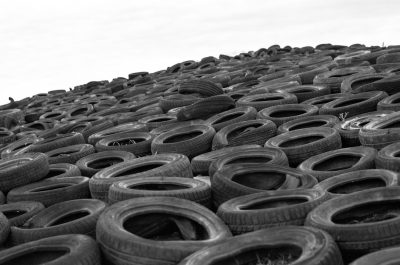 A black and white photograph of an endless pile of used tires, symbolizing the environmental impact of car traffic. The scene is captured from above with a wide-angle lens to emphasize the scale of industrial waste against a plain background. --ar 32:21