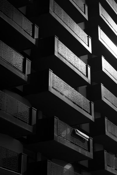 modern high rise building with balconies, geometric patterned metalwork, architectural photography, black and white photography, low angle shot, night scene, soft light from the right side of frame, contrast lighting, hard shadows, strong visual flow --ar 85:128