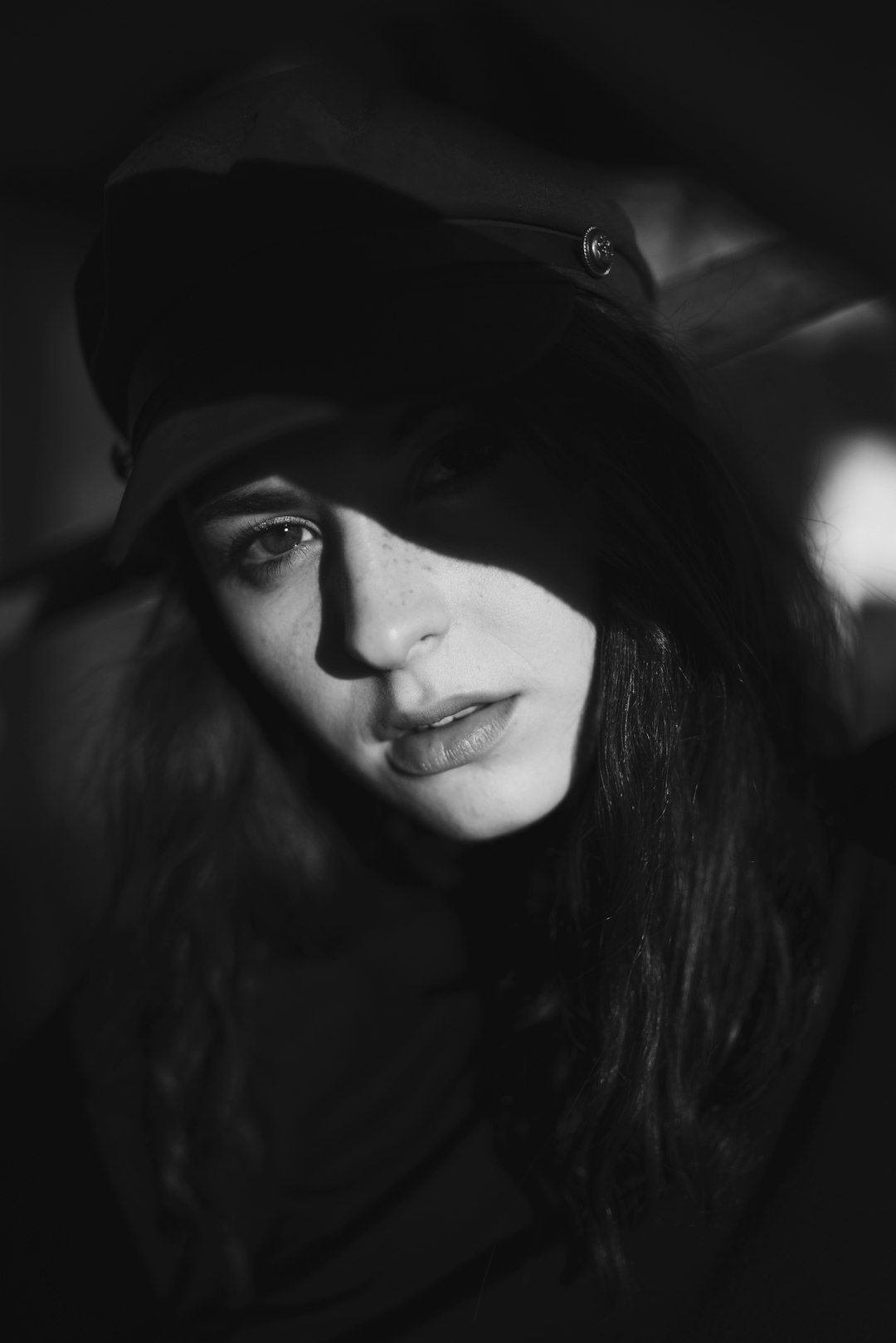 Black and white portrait of a woman wearing a cap, with high contrast and hard shadows, shot on a Sony A7R with an f/2 lens in the style of film noir. –ar 85:128