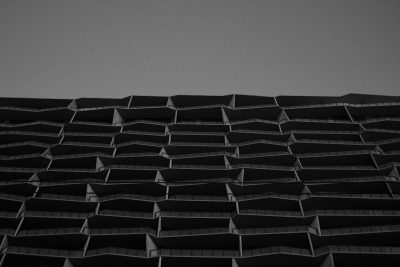 A black and white photograph of an abstract building with angular balconies, reminiscent of the honeycomb patterned style seen in the style of Mamiya's photography work. The building is set against a clear sky background, emphasizing its architectural design. --ar 128:85