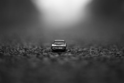 Black and white macro photo of a toy car on an asphalt road, with a blurred background, depth of field effects, high contrast, soft light, minimalist and clean style, simple composition, dark tones, low angle view, shallow focus achieved with a macro lens, shallow focal point, captured with a Nikon D850 in the style of minimalist photography. --ar 128:85