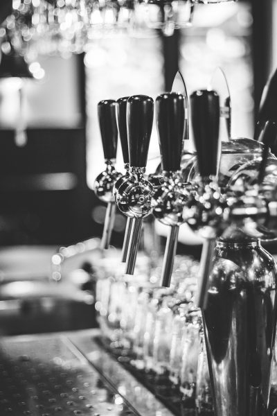 black and white photo of a beer tap at a bar with multiple black and silver beer taps instead of glasses on the counter, shot from behind in the style of a canon eos r5 --ar 85:128