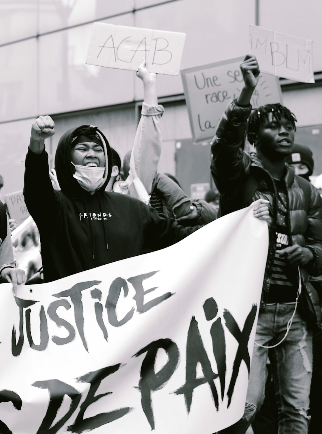 A group of people holding signs and banners with the words “bachelor justice de pan” written on them, a black man wearing a hoodie standing in front of a police station waving a hand painted banner saying one set of rules for race and another for brm, a low angle shot, editorial photography in the style of 24mm f/8 black and white film photography, street style photo. –ar 95:128