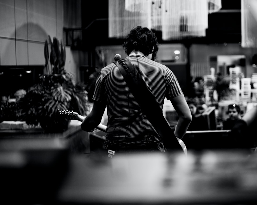 Photo of the back view, from behind, of an American man in his thirties with dark hair and wearing jeans standing at a restaurant counter playing guitar for people eating inside the restaurant. Black and white, in the style of Hasselblad photography, shallow depth of field, highly detailed photo, hyper realistic. –ar 64:51