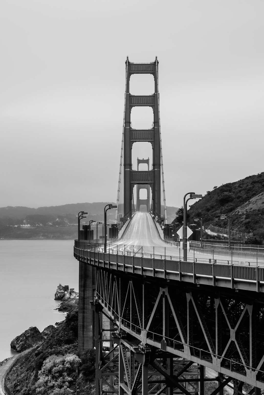 Golden Gate Bridge, San Francisco, California, USA. , Black and white photography, high definition, photography style, Fujifilm XT4, f/8 aperture, 35mm lens, grainy film filter, black bridge with white road on the side of it, white guard that is about to cross over in front of camera, gray sky, ocean view in background. –ar 85:128