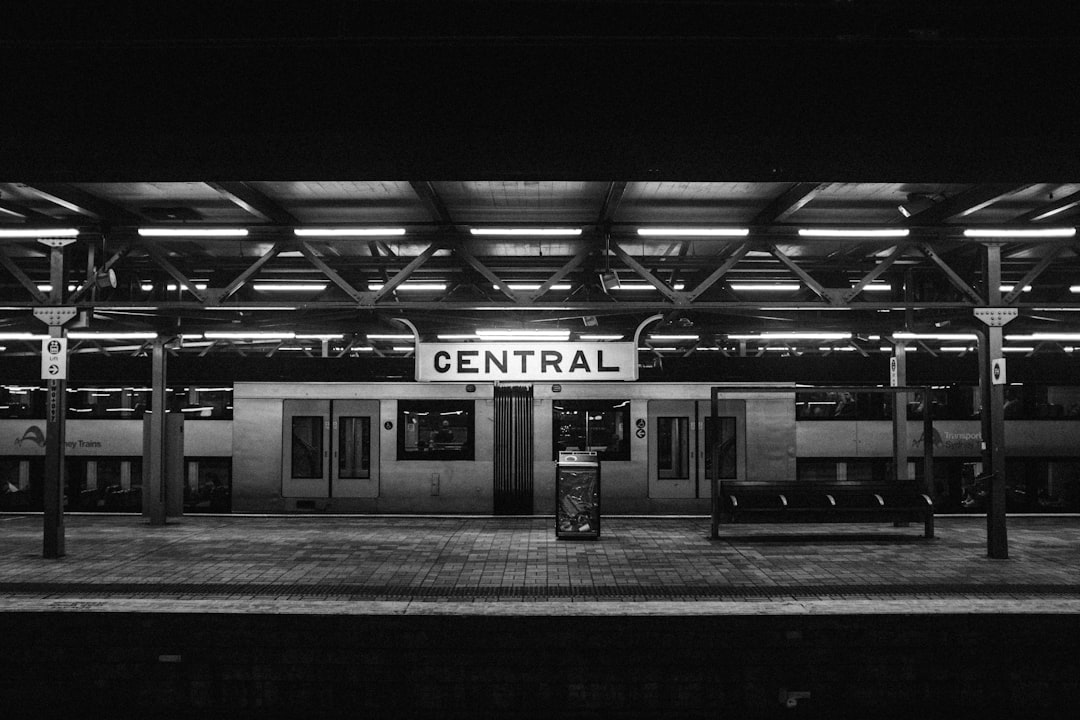 A black and white photograph of the central train station in Slee, New York City at night. The platform is empty with no people or vehicles present. A large sign on top reads “Rica.” There is an open door leading to another room. In front there are two rows of benches. It was taken in the style of photographer Karyn Linen from inside looking out through the glass ceiling. This shot gives off an eerie feeling as it seems abandoned. –ar 128:85