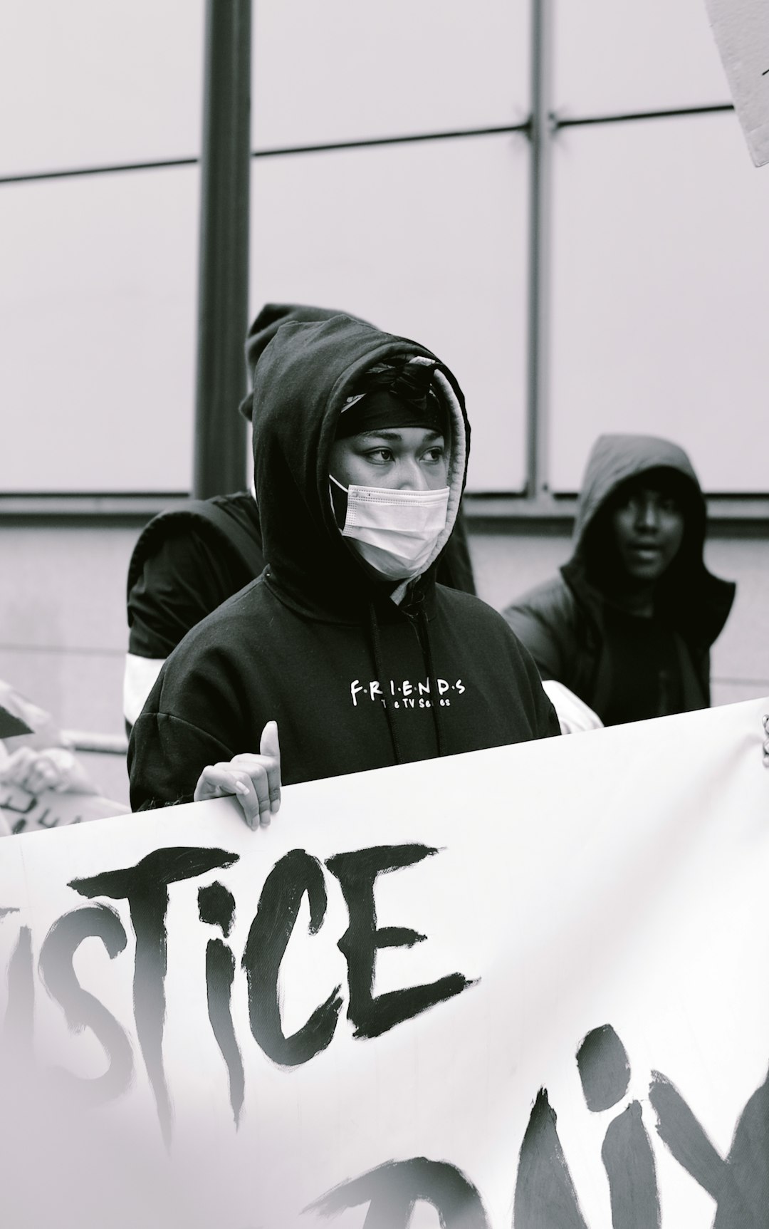 Photo of a black and white hooded young man wearing a mask on his face holding a banner that says “,请.” with a group of people in hoodies standing behind him, holding signs saying justice. The photo was shot in the style of ARRIFLEX35 BL camera, with photographic quality. –ar 5:8