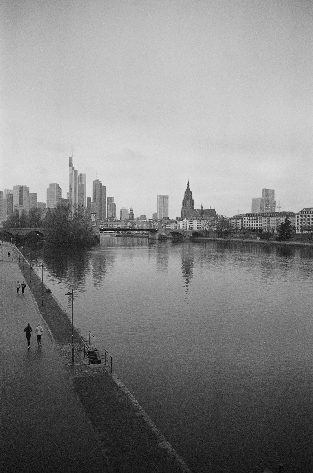 FrankGabersh, a black and white photograph of the skyline in the style of frank component036 with people walking along the mainz river. –ar 21:32