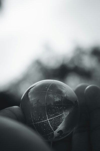 A closeup of a glass globe held in the hand, with mountains and rivers visible inside. The background is blurred to emphasize the foreground object. The photography style is black and white. High contrast between light and dark tones creates strong texture. Soft side lighting highlights details on the earth's surface. Shot from an overhead perspective using a Nikon D850 camera. --ar 85:128