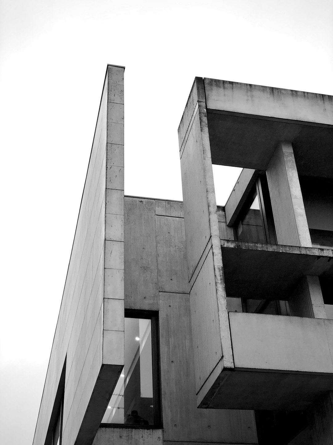 A black and white photo of the side view of an architectural building, showcasing brutalist design elements with sharp angles and concrete structures. The focus is on one corner where two different cube shapes meet to form interlocking geometry patterns. There’s no sky in sight, just solid grey color. –ar 3:4