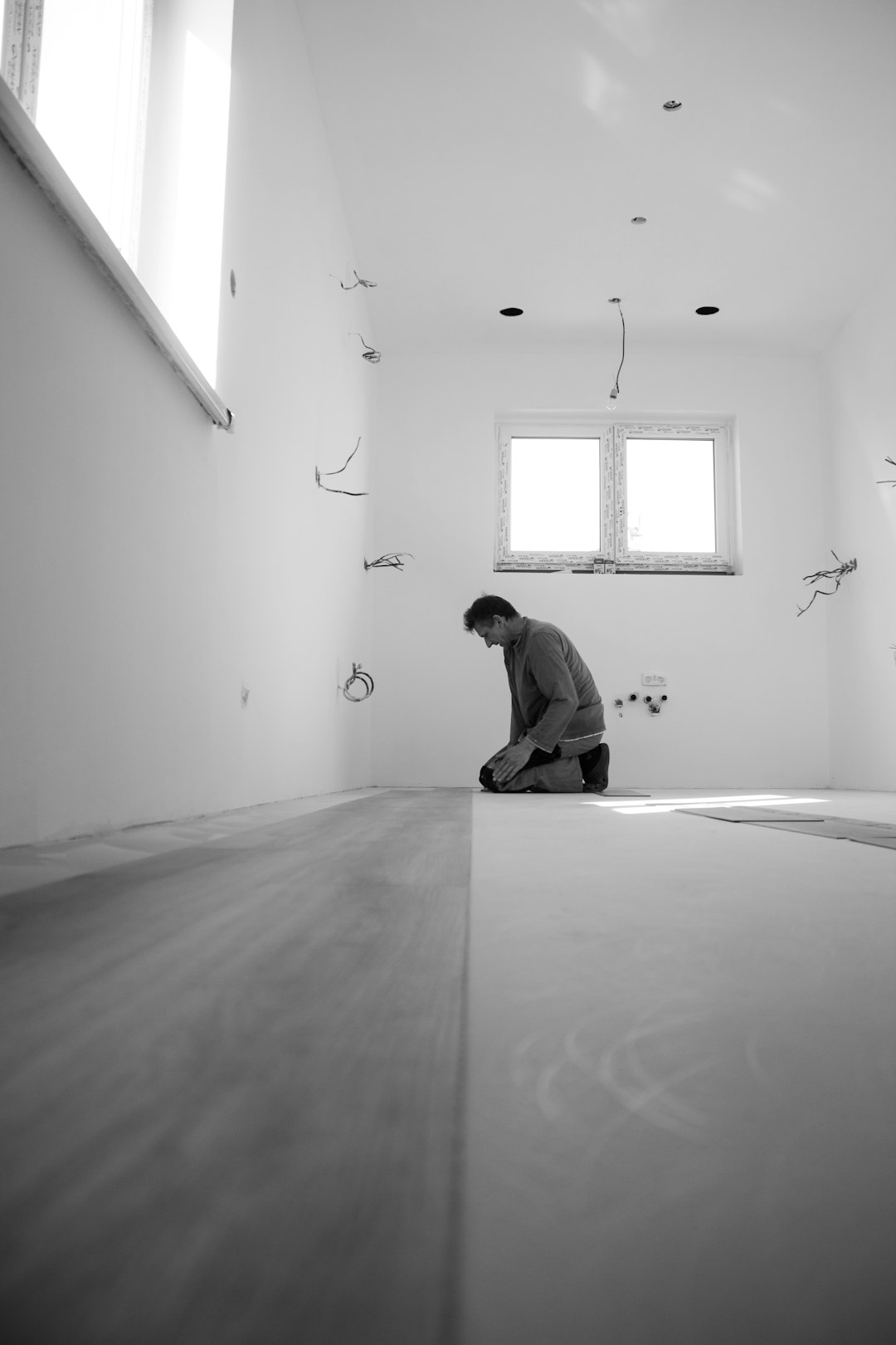 A photo of a carpenter laying parquet in the middle of a room, with empty walls, in black and white photography, taken with a wide shot from a high angle view, in the style of unsplash photography, with a minimalistic style. –ar 85:128