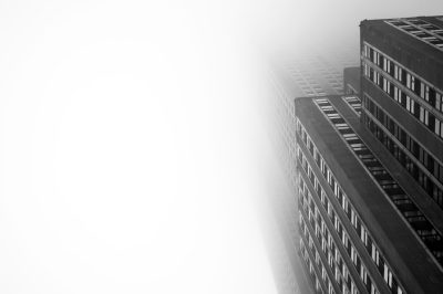 A black and white photograph of the exterior wall of an office building in New York City, partially obscured by fog. The photo captures only two floors above ground level. There is no sky visible. The atmosphere should be moody with soft light filtering through the mist, creating a sense of mystery and depth. The focus will land on one side or another of that part of buildings, creating visual interest and adding to the overall mood. The photograph should be taken in the style of high resolution photography. --ar 128:85