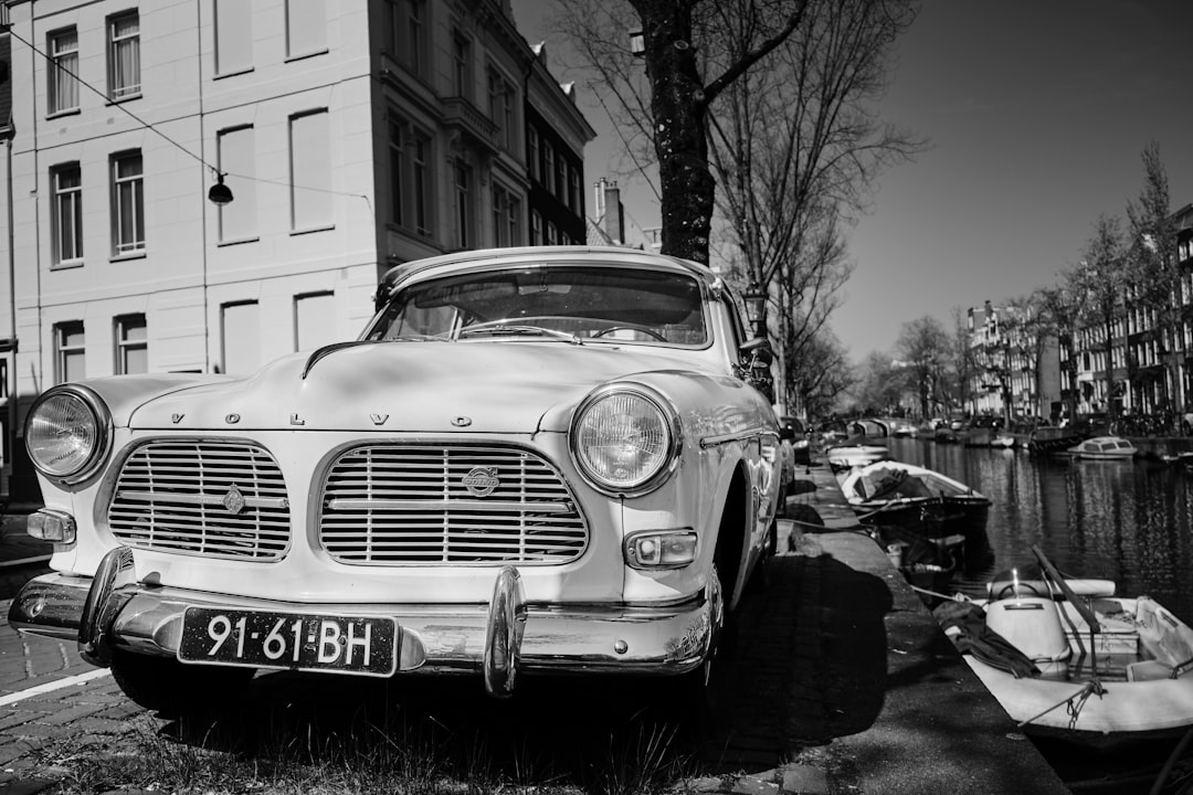 Black and white photo of an old “, beautiful, classic” volvo p230 parked on the side of amsterdam canal in springtime. The car has no license plate. Shot with hasselblad camera –ar 128:85