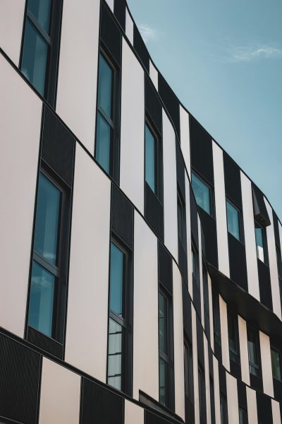 A closeup photo of the curved facade, showcasing its vertical black and white stripes with an elegant touch. The building's architecture is in a modernist style, featuring large windows that showcase the surrounding urban landscape. This composition highlights the unique patterned design on one side of the structure, creating visual interest against the clear blue sky background. Shot in the style of Sony Alpha A7 III, 35mm lens at f/2.8 aperture, ISO 400 for balanced exposure. --ar 85:128