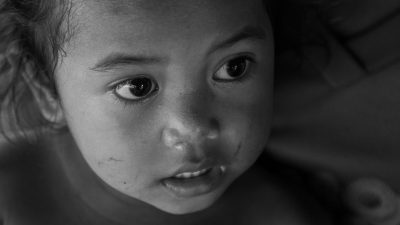 A black and white portrait of an Asian child crying, tears on her face, the photo is taken from above, the focus point should be just under her eyes. The background should have some light in it but not too much. Shot with a Canon EF 24-70mm f/5 L IS USM wide angle lens at F8, ISO 63, 9s shutter speed, in the style of a portrait. --ar 16:9