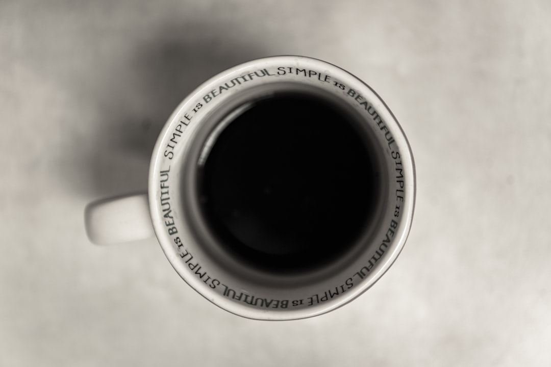 A black and white photo of the text “Srecipe is beautiful” written on top of a coffee mug, seen from above and centered in the middle of the cup. It is an overhead view and close up shot with a simple background. The photo has a monochrome and high contrast style with a minimalist and vintage feel. It has clear focus with a top-down perspective at high resolution and high detail, depicted in the style of hyper realistic. –ar 128:85