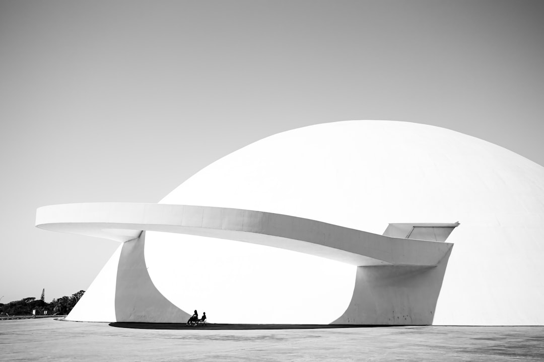 Black and white photography of the National Theater in Brazil tourists watching an open-air concert on top of it, designed in the style of [Oscar Niemeyer](https://goo.gl/search?artist%20Oscar%20Niemeyer) with two giant concrete domes, minimalist architecture, iconic photo, minimalism. –ar 128:85