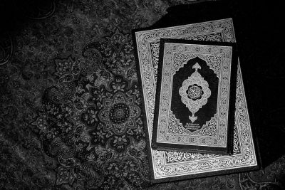 Black and white photograph of the two holy books, the Quran and Bible, on top of an Islamic pattern rug, with high resolution and intricate details, in the style of cinematic photography with cinematic lighting, dramatic shadows, and dynamic light reflections. --ar 128:85