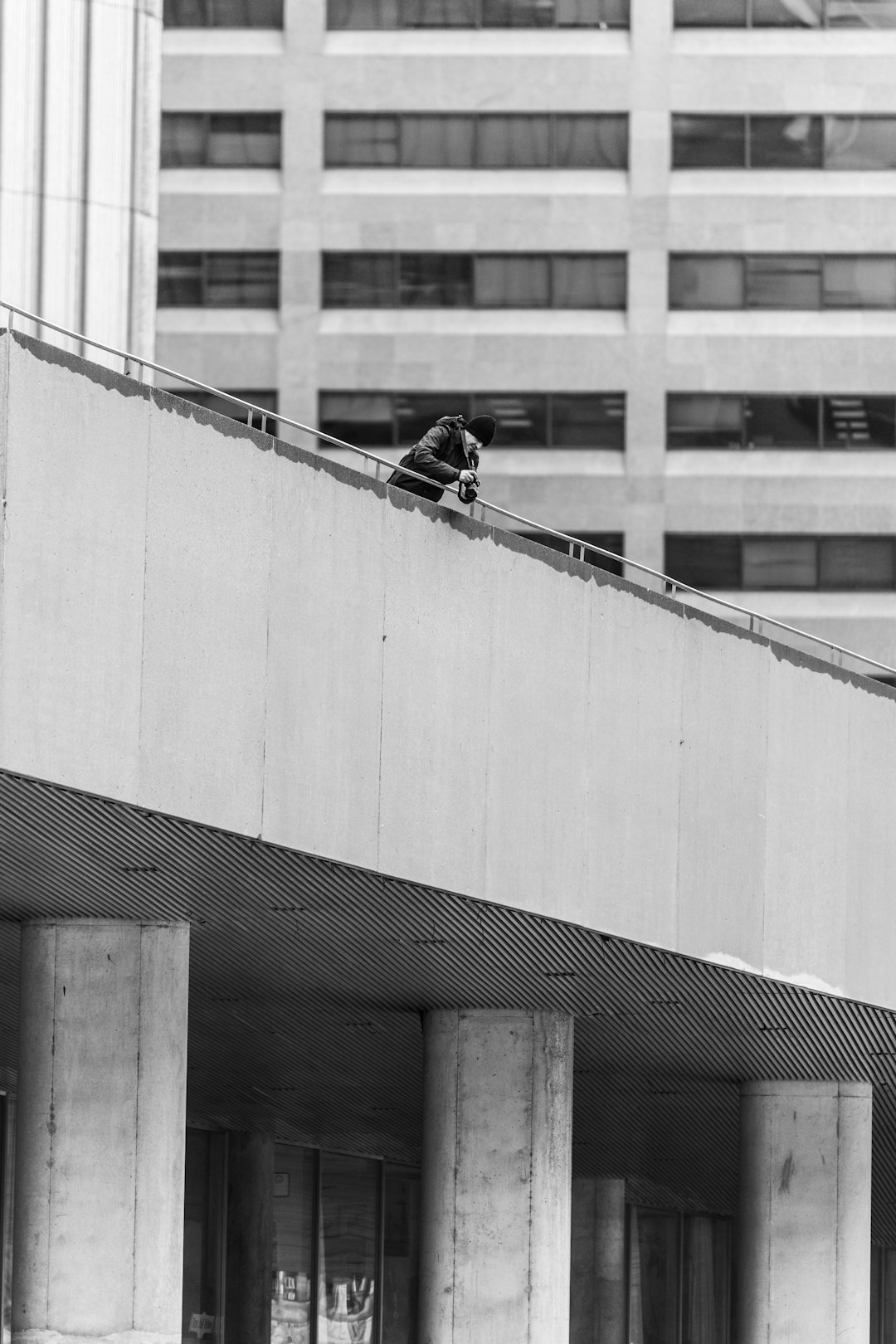 A man is crouching on the edge of an office building, trying to do parkour while holding his phone and taking photos with it. The scene takes place in downtown Montreal’s financial district, captured in the style of Leica M6 using Ilford HP5 film. –ar 85:128