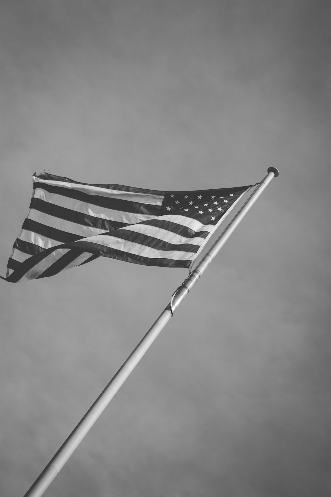 A black and white photo of an American flag waving in the wind on top of a pole in the style of unsplash photography. –ar 85:128