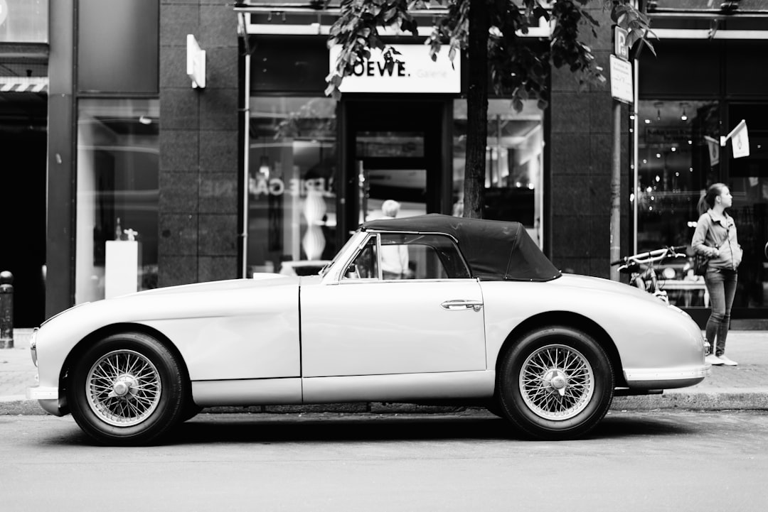 Side view of a white vintage sports car parked in front of a modern fashion store, in the style of street photography, using black and white film stock. –ar 128:85