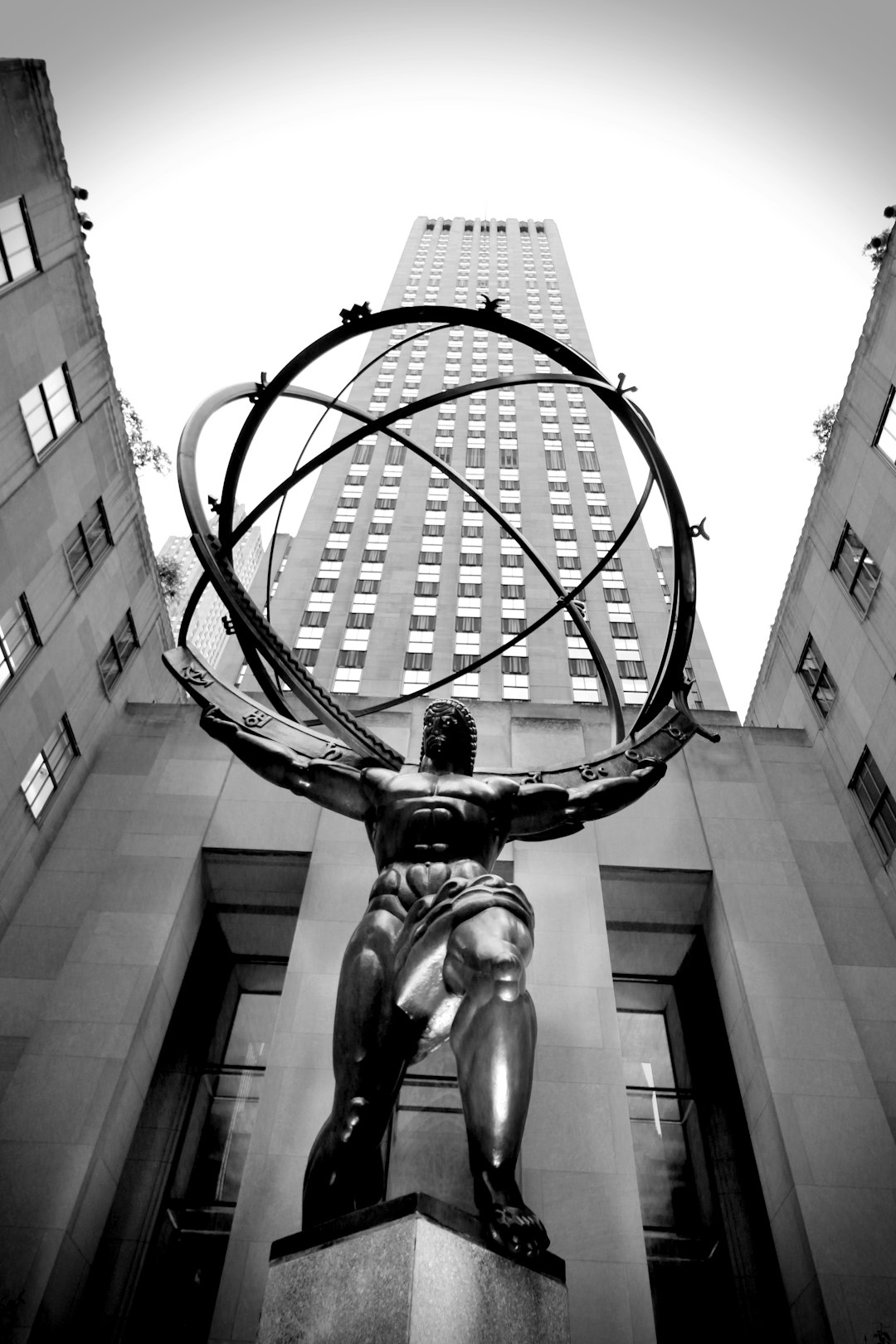 Black and white photo of Rockefeller Center in New York City, featuring an antique statue of Der Gmented eôtel with a giant metal sphere around it, wide angle view, low angle shot, in the style of unsplash photography. –ar 85:128