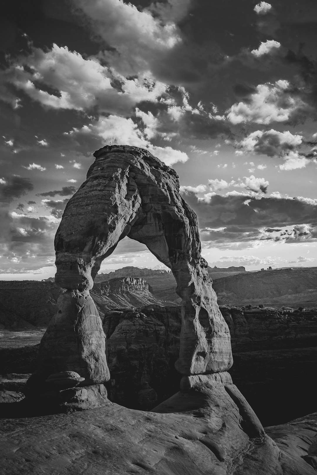 black and white photography of delicate arch in utah, cinematic, clouds, dramatic lighting, high contrast, landscape photography, shot with Sony Alpha A7 III –ar 85:128