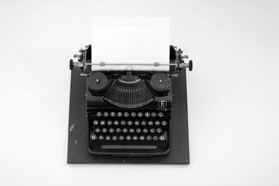 Black and white photograph of an old typewriter with paper, on a plain background. The focus is sharp to capture the details of each key in black ink against a stark white backdrop. This creates contrast that emphasizes both the classic design of the machine and its historical significance as a symbol for storytelling through text --ar 128:85