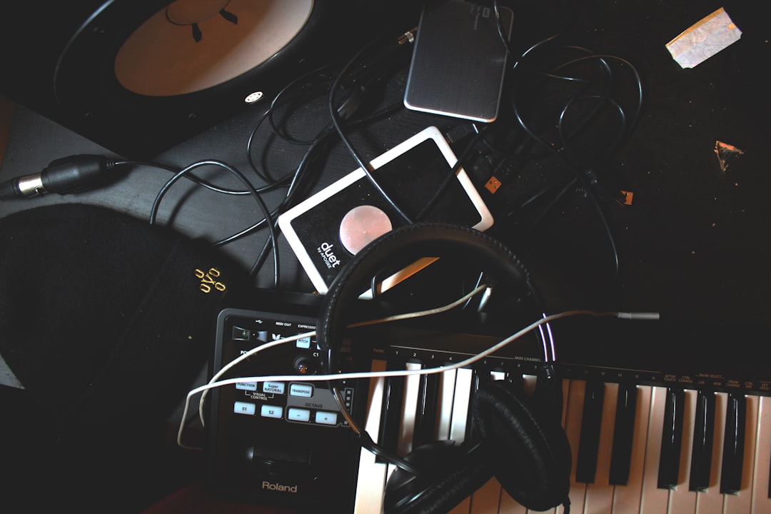 A black table with an iPhone, digital mixing equipment and headphones is shown. On the side, piano keys, a Roland drum machine and two musical tablets with notes are also visible. The top view is in the style of unsplash photography. –ar 128:85