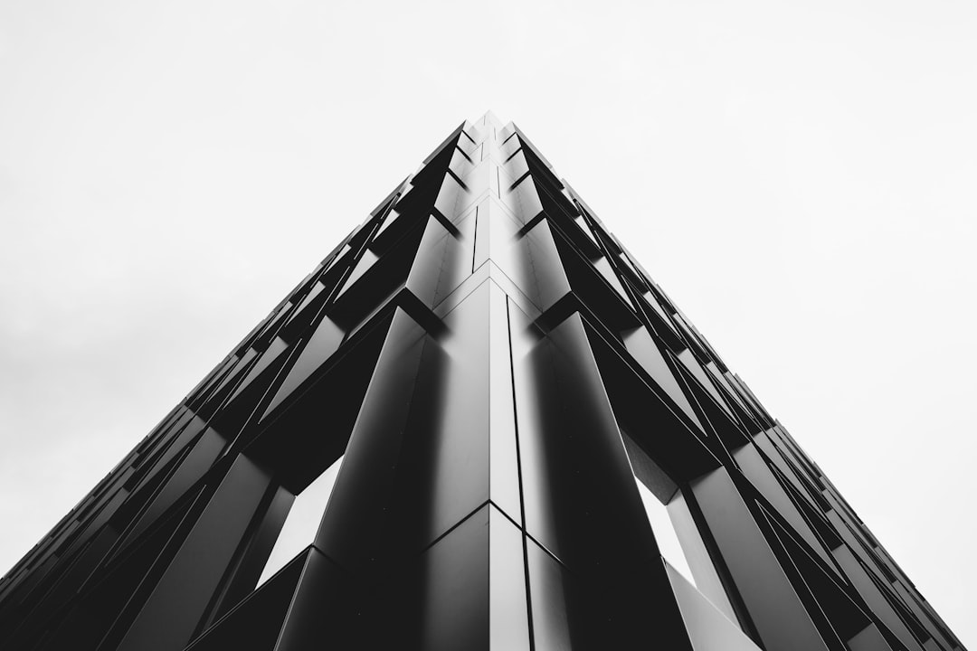 A sleek, geometric skyscraper against the stark white sky, captured from an upward angle to emphasize its towering presence and modern architecture. Black & White Photography with attention to detail in architectural design. Shot in the style of David trash polflower. –ar 128:85