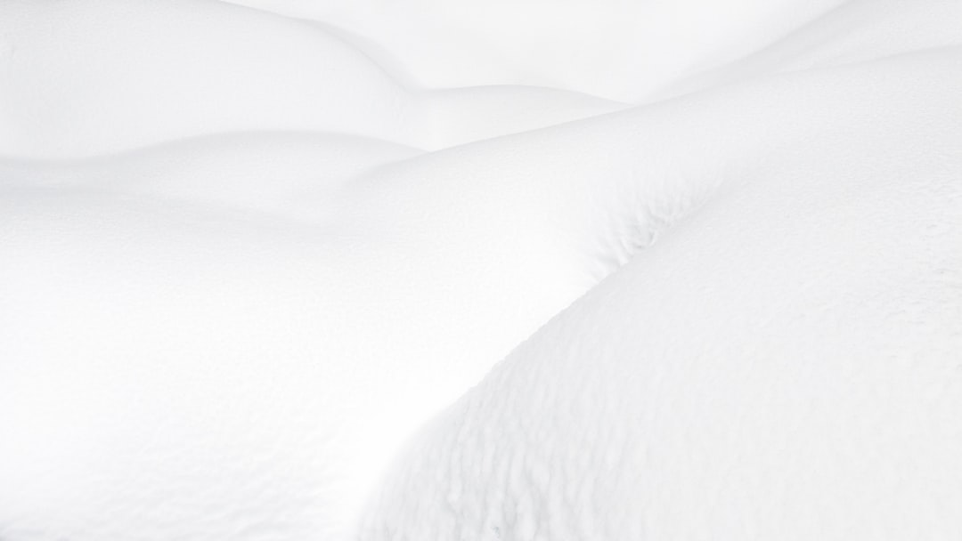 A closeup of snow-covered dunes, with soft lines and curves that resemble the shape of an arm or leg lying down. The white background is a pristine gradient from light to dark tones, creating a sense of depth in the snowflakes. This minimalist composition emphasizes simplicity and elegance, evoking feelings of calmness and tranquility in the style of minimalism. –ar 16:9