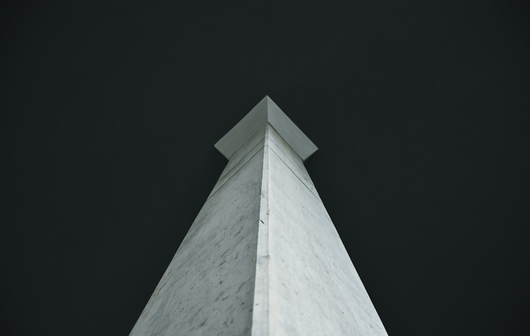 Low angle photo of a white marble obelisk against a dark background, shot from below in a minimalist style. The photo was taken with a Fujifilm Pro 800Z film in the style of Hassano S75’s photography. –ar 128:81