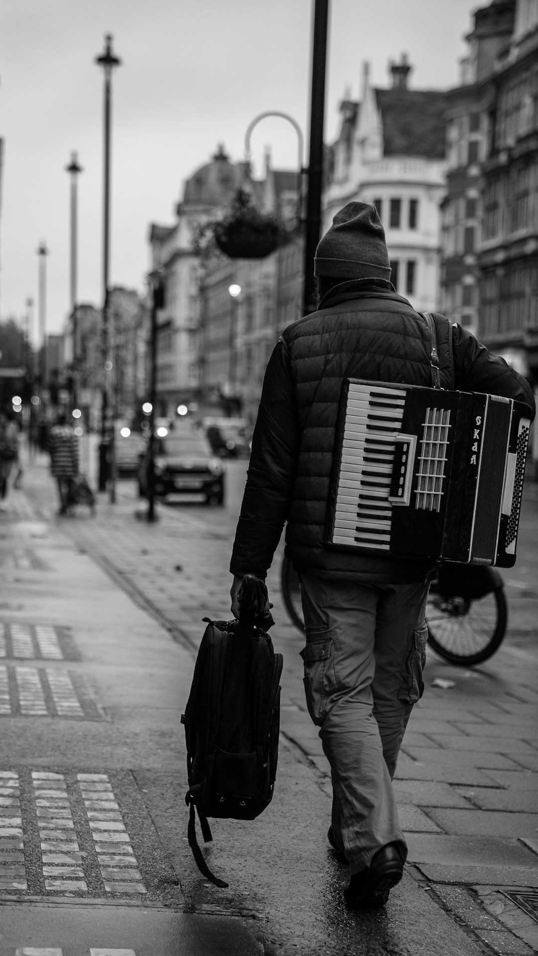 A man walking down the street with an accordion case on his back, in the style of black and white photography, street photography, london city, wide angle shot. –ar 9:16