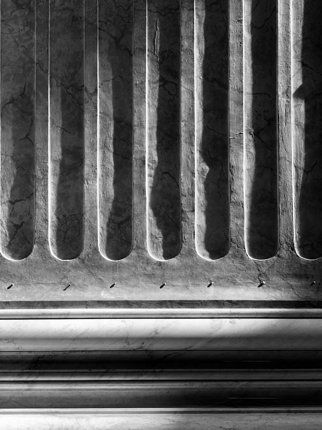 A close up of the bottom edge of an ancient Greek column, the shadows cast in the style of the light from above form vertical lines on the marble, black and white photography, grainy. –ar 3:4